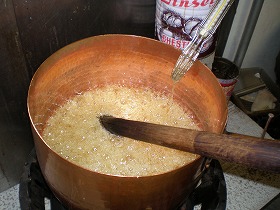 当社の飴はすべて、大きな銅製の鍋に原料（砂糖、水飴）を入れ、直接底から火をあてて、煮詰めて水分をとばし飴にする直火炊き製法です